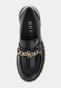 Czarna lakierowana skórzana mokasyna z złotym łańcuszkiem i detalem z logo. Posiada zaokrąglony nosek i teksturowaną podeszwę. Gładka powierzchnia.