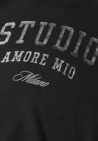 Tissu noir avec texte imprimé en blanc indiquant STUDIO, AMORE MIO et Milano dans différentes polices et styles.
