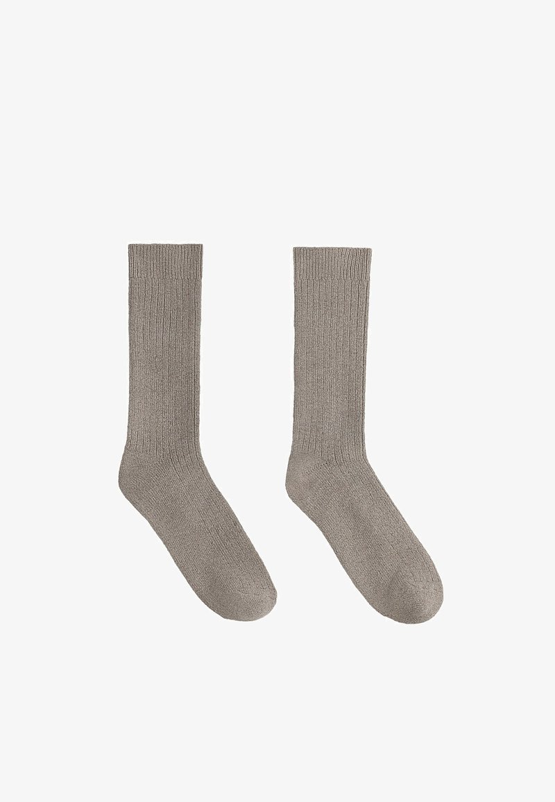Paire de longues chaussettes en tricot côtelé gris clair, posées à plat avec les orteils pointant vers le bas sur fond blanc.