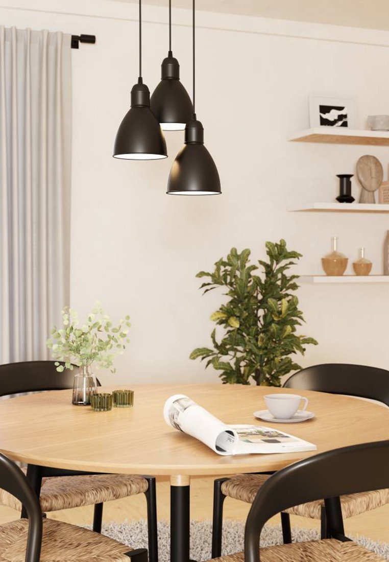 Drei schwarze Pendelleuchten hängen über einem runden Holztisch. Der Tisch hat geflochtene Sitze und eine Pflanze in der Nähe, mit einer Zeitschrift und einer Tasse darauf.