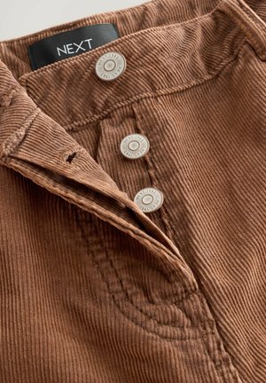 Bruin corduroy stof met verticale ribbels, voorzien van twee zilveren knopen en een zwart label gemarkeerd "NEXT" op de tailleband.
