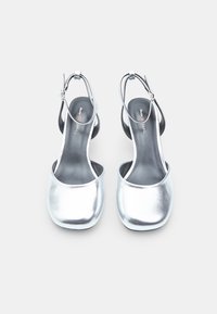 Hopeisiin metalliset slingback-kengät, joissa on pyöreä kärki, sileä pinta ja säädettävä nilkkaremmi; tyylikäs ja minimalistinen muotoilu.