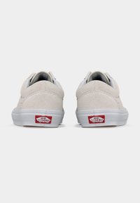 Ζευγάρι μπεζ σουέντ αθλητικά παπούτσια Vans, εμφανιζόμενα από πίσω, με κόκκινο λογότυπο "Vans Off The Wall" στις λευκές λαστιχένιες σόλες.