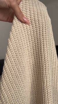 Κρεμ ύφασμα πλεκτό με υφή και ανοιχτό σχέδιο. Το υλικό φαίνεται μαλακό και ευλύγιστο, αναδεικνύοντας μια χαλαρή, αέρινη ποιότητα.