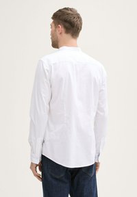 Camicia bianca a maniche lunghe con vestibilità rilassata, colletto button-down e maniche con polsini, abbinata a jeans in denim scuro. Texture liscia.