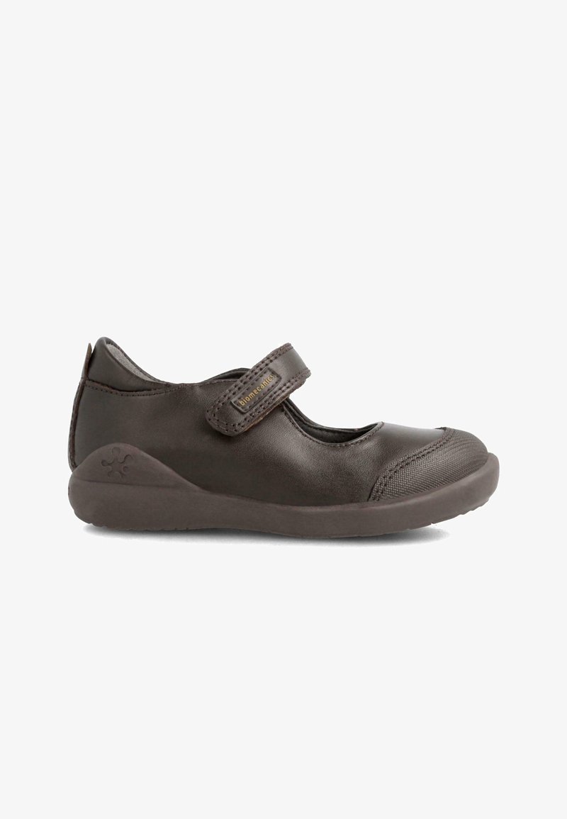 Zapato Mary Jane de cuero marrón con una correa de velcro, puntera redondeada y tapa de puntera texturizada. Presenta una suela de goma y un logotipo grabado en el talón.