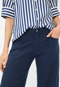 Navy blue pants in a smooth, stretchy fabric. Features a front pocket, belt loops, and a button closure. Paired with a blue and white striped shirt.