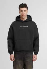 Svart hoodie i mjukt tyg, med en framfickan och texten "STARTADE FRÅN BOTTEN." tryckt i vitt.