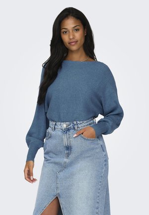 Pull en maille bleu avec un col large et des manches ballons, associé à une jupe en denim taille haute avec une fente à l'avant.