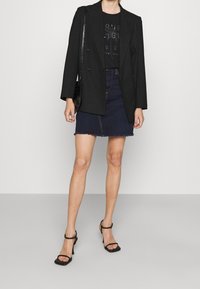 Black double-breasted blazer with wide lapels, paired with a fitted black graphic T-shirt and a dark denim skirt with frayed hem. Black strappy heels complete the look.