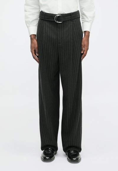 Donkergrijze pantalon met een brede broekspijp en een riem met gesp, gemaakt van een gestructureerde stof. Zwarte schoenen maken de outfit compleet.