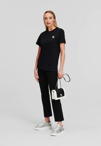 Černé tričko s krátkým rukávem, zdobené malým zlatým logem, doplněné černými kalhotami, stříbrnými teniskami a černobílou kabelkou.