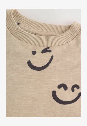 Beżowy sweter bawełniany z prążkowanym kołnierzem, zdobiony dwoma czarnymi nadrukami uśmiechniętej twarzy. Miękka tekstura i casualowy design.