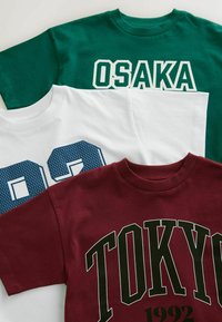 Drie katoenen t-shirts: donkergroen met "OSAKA" in het wit, wit met "92" in blauwe mesh, en kastanjebruin met "TOKYO 1992" in vet groen.