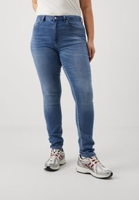 Modre skinny jeans iz denima imajo srednje visok pas, klasičen pet-pocket dizajn in rahlo zbledelost. V kombinaciji z metalnimi športnimi copati.