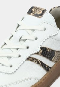 Λευκό δερμάτινο αθλητικό παπούτσι με υφασμάτινη επιφάνεια, αντικρουόμενες μαύρες και μπεζ λεπτομέρειες με σχέδιο φιδιού και μπεζ εξωτερική τακούνι από καουτσούκ. Κανονικό σύστημα κορδονιών.