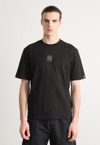 T-shirt nera a maniche corte in cotone con colletto rotondo, caratterizzata da un piccolo logo grafico sul petto e una serigrafia discreta sul maniche.