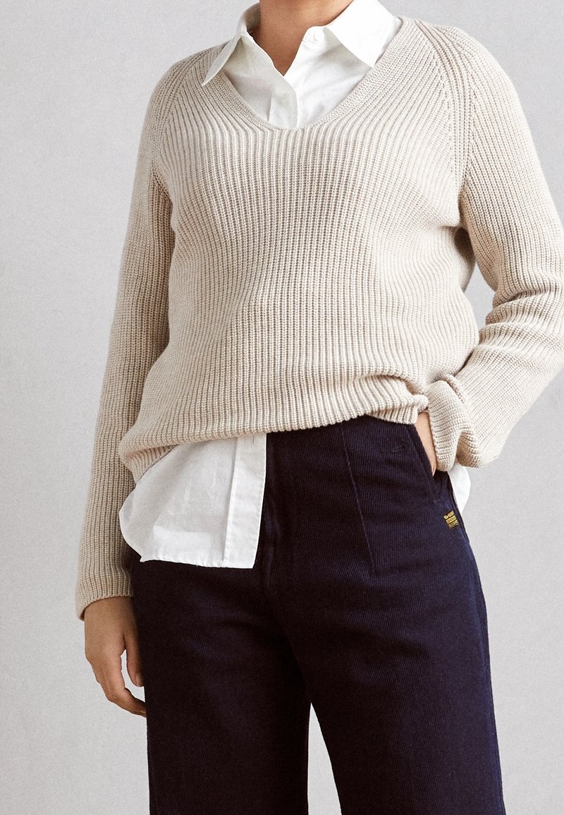 Beige geribbelde gebreide trui met een V-hals, gedragen over een frisse witte overhemd met kraag, gecombineerd met donkergroene corduroy broek voor een gestructureerde uitstraling.