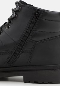 Bota de cuero negro con un acabado texturizado, que presenta ojales de metal, costuras en contraste y una cremallera lateral para un fácil acceso.