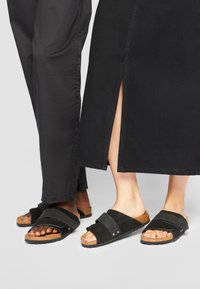 Czarne zamszowe klapki na korkowej podeszwie z dwoma szerokimi paskami. Teksturowana cholewka, otwarty nos i casualowy styl, odpowiednie do różnych outfitów.