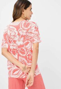 Korallenfarbenes Kurzarm-Top mit weißen Blumen- und Blättermustern, aus leichtem Stoff, mit lockerem Schnitt und abgerundetem Ausschnitt.