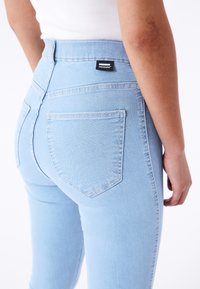 Jeans skinny de mezclilla azul claro con una cintura alta, que cuentan con bolsillos traseros y una etiqueta de marca negra en la cinturilla. Textura suave.