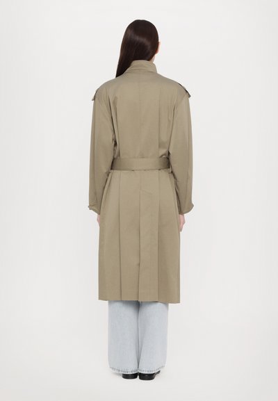 Khaki trench coat with a belted waist, long sleeves, and shoulder epaulets; paired with light blue wide-leg jeans.