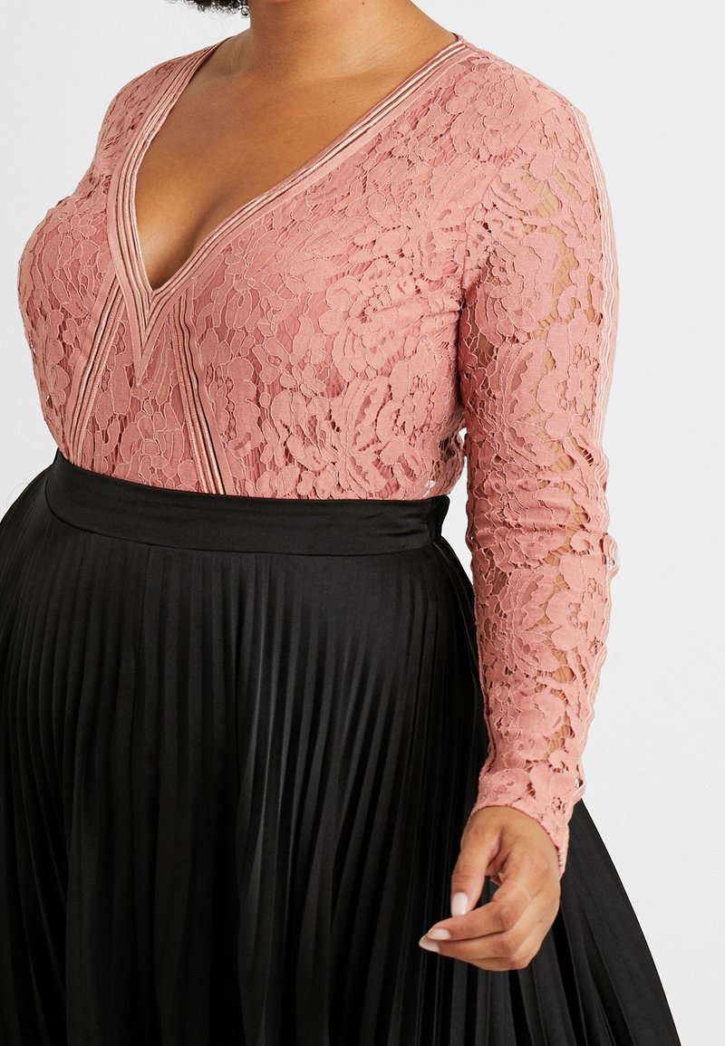 Body in pizzo di un delicato rosa con maniche lunghe e scollo a V profondo; abbinato a una gonna plissettata nera con un ampio elastico in vita.