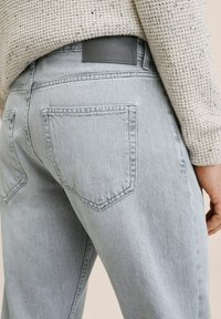 Jeans di denim grigio chiaro con vestibilità slim, caratterizzati da due tasche posteriori, cuciture sottili e una toppa in pelle grigia sulla cintura.