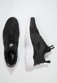 Black Nike Air Huarache sneakers featuring breathable mesh, a textured upper, and a white sole with a distinctive heel tab.