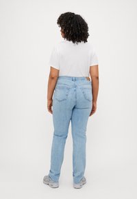 Jeans de denim azul claro con una cintura ligeramente alta, diseño de cinco bolsillos y detalles de costura sutiles, combinados con una camiseta blanca y zapatillas grises.