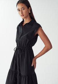 Must musterta kleit nupuväärse esiosaga, elastse vöökoha ja kokku volditud seelikuga. Valmistatud siledast kangast, klassikalise kraega.