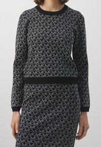 Maglione nero a maglia con un motivo geometrico grigio ripetuto, dotato di scollatura a girocollo e polsini e orlo neri a coste.
