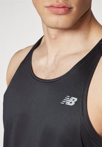 Black athletic tank top made of textured fabric, featuring a rounded neckline and a reflective logo on the left chest area.