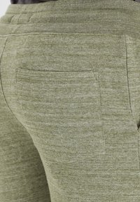 Pantaloni della tuta verde oliva realizzati in tessuto morbido e testurizzato, con una tasca sul retro, cintura a costine e dettagli di cucitura.