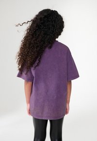Överdimensionerad lila bomullströja med mjuk textur, rundad halsringning och korta ärmar; stylad med glänsande svarta leggings.