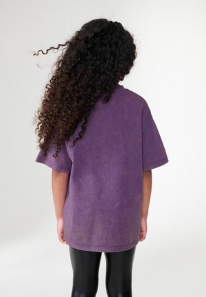 Übergroßes lila Baumwoll-T-Shirt mit weicher Textur, Rundhalsausschnitt und kurzen Ärmeln; kombiniert mit glänzenden schwarzen Leggings.