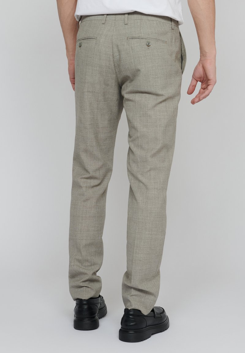 Jasnoszare spodnie wykonane z teksturowanej tkaniny. Posiadają dwie tylne kieszenie zapinane na guziki oraz dopasowany krój. Widać czarne buty.