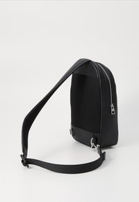 Black backpack with a textured, mesh surface and smooth leather base. Features a zippered closure and adjustable strap for versatile wear.