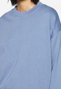 Sudadera de gran tamaño en azul claro con cuello redondo, confeccionada en suave tejido de algodón y con costuras de hombro caídas para un ajuste relajado.