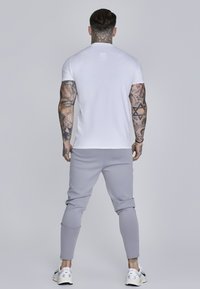 Hvid kortærmet t-shirt parret med lysegrå tapered joggingbukser, der har en glat tekstur og elastiske manchetter, båret med hvide sneakers.