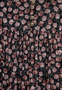 Robe à imprimé floral présentant de petites fleurs roses et crème sur un fond noir, jupe plissée et cinq boutons décoratifs sur le devant.