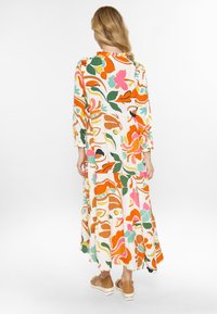 Langes, gestuftes Kleid aus leichtem Stoff mit einem lebhaften Blumenmuster in Orange, Pink, Grün und Creme, mit langen Ärmeln und einem gerüschten Ausschnitt.