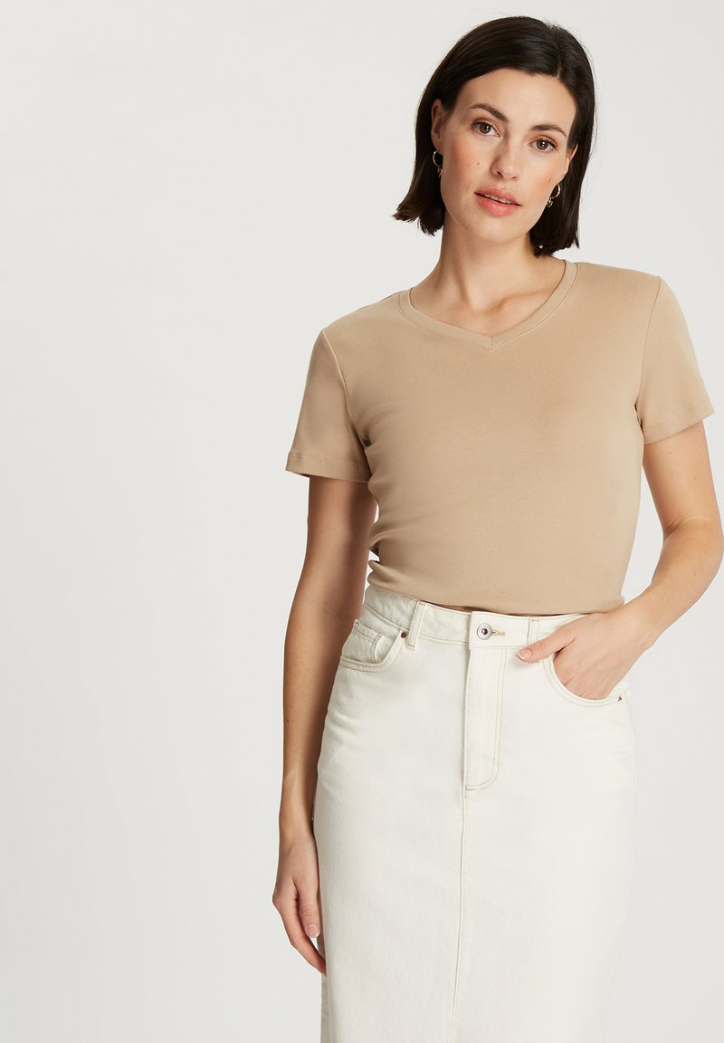 Koszulka z krótkim rękawem w odcieniu beżowym, z dekoltem w serek, wykonana z miękkiego materiału, zestawiona z białą spódnicą dżinsową o wysokim stanie z zapięciem na guziki z przodu.