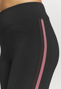 Svarta leggings gjorda av slitstark, elastisk tyg med hög midja och vertikala ränder i mörkrosa och ljusrosa på sidan.