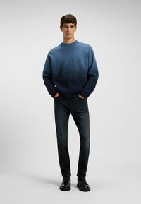 Suéter de cuello redondo de punto en tonos azules degradados, con un acabado texturizado y puños acanalados, combinado con jeans oscuros y botas negras.