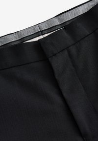 Pantaloni neri a vita alta con una texture liscia, caratterizzati da una cintura a motivo a quadri e cuciture precise lungo le cuciture e i bordi.