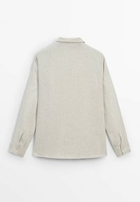 Chemise beige à manches longues avec col, poignets boutonnés et dos uni, présentée sur fond blanc.