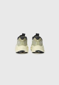 Pair of beige and black sports shoes shown from the back, featuring thick white soles and Puma logos on heels and soles.