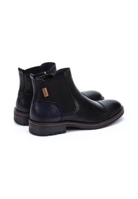 Botas de tobillo de cuero negro con paneles laterales elásticos, punta redondeada, tacón bajo y una etiqueta decorativa. Textura duradera y un acabado pulido.